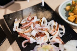 Cooked squid tentacles and rings on a black plate.