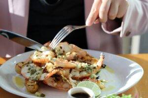 Person eating grilled shrimp with lime and sauce